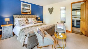Une chambre à coucher comprenant un lit, deux tables de chevet, une chaise, une petite table ronde avec des tasses, un miroir et une porte donnant sur une salle de bain.