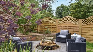 Une terrasse avec des meubles en osier, un foyer extérieur et une clôture en bois.
