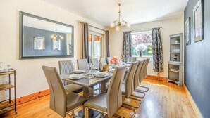 Une salle à manger avec une longue table, des chaises, un lustre et une vue sur l’extérieur.