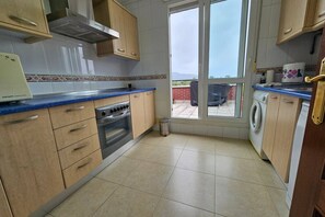 A kitchen with wooden cabinets, a built-in oven, a washing machine, and a view through a glass door.