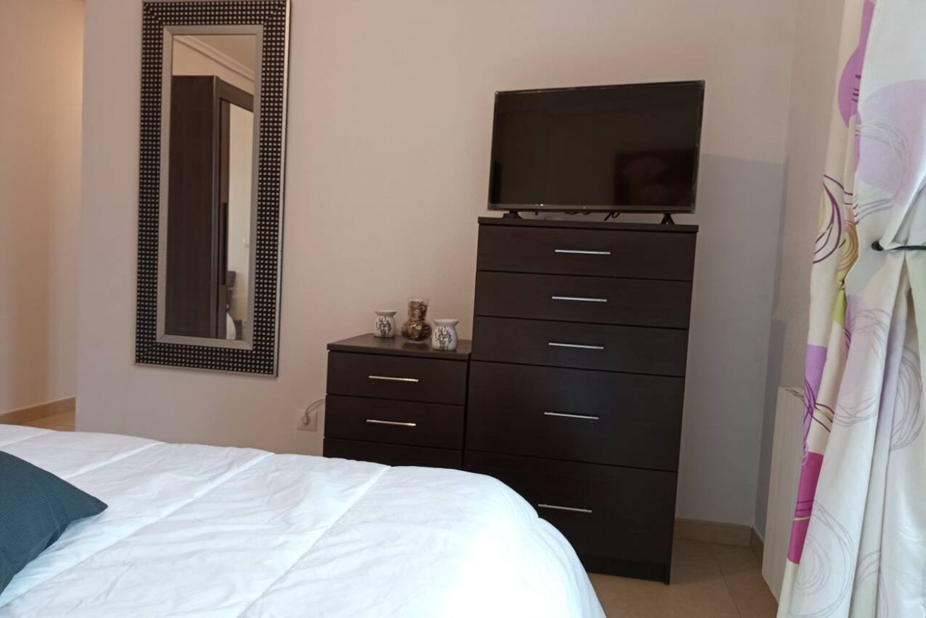 Een slaapkamer met een bed, een dressoir, een televisie en een spiegel.