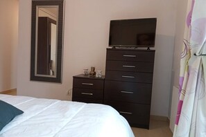 Un dormitorio con cama, cómoda, televisor y espejo.