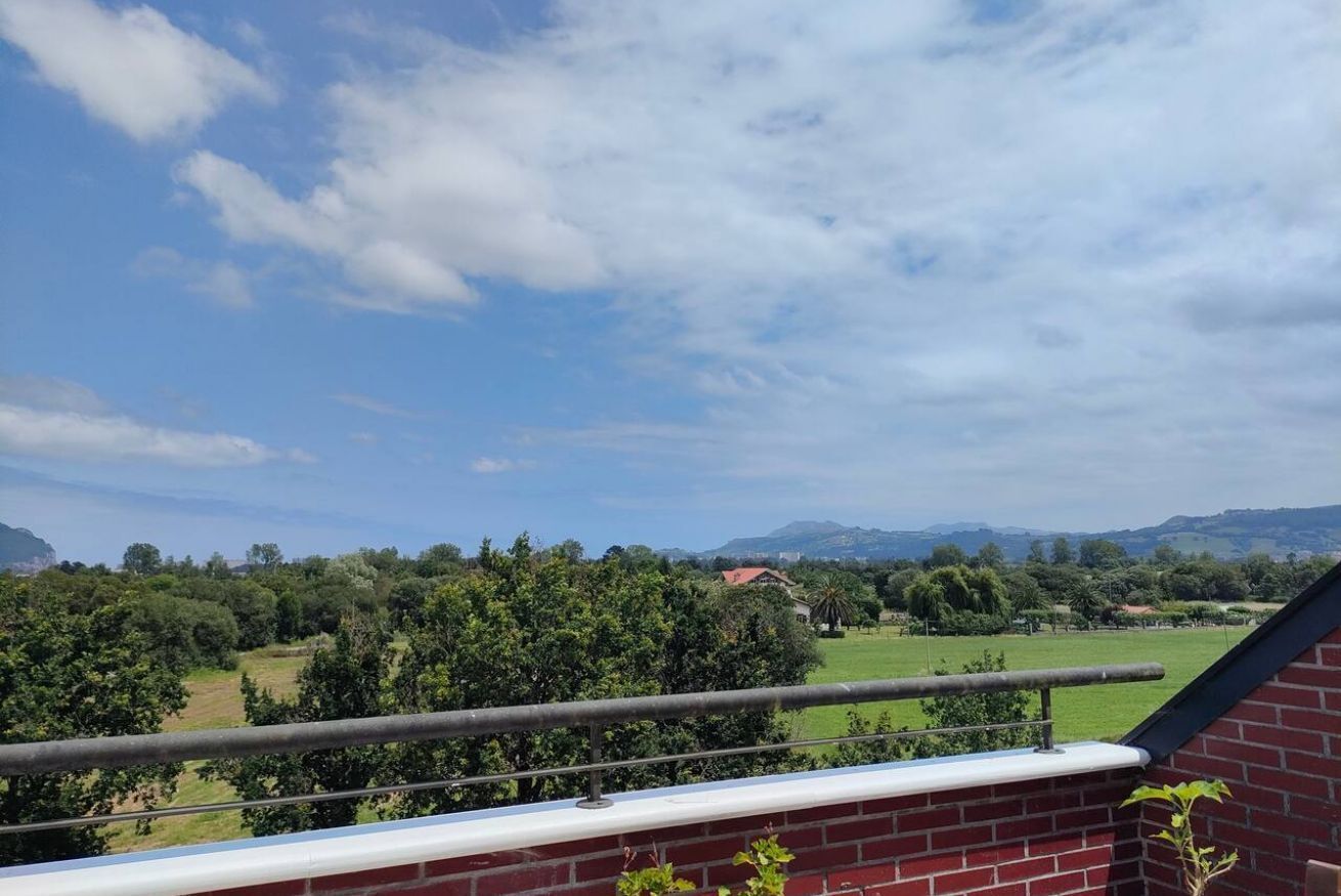 A balcony with a view of a green landscape and distant mountains.