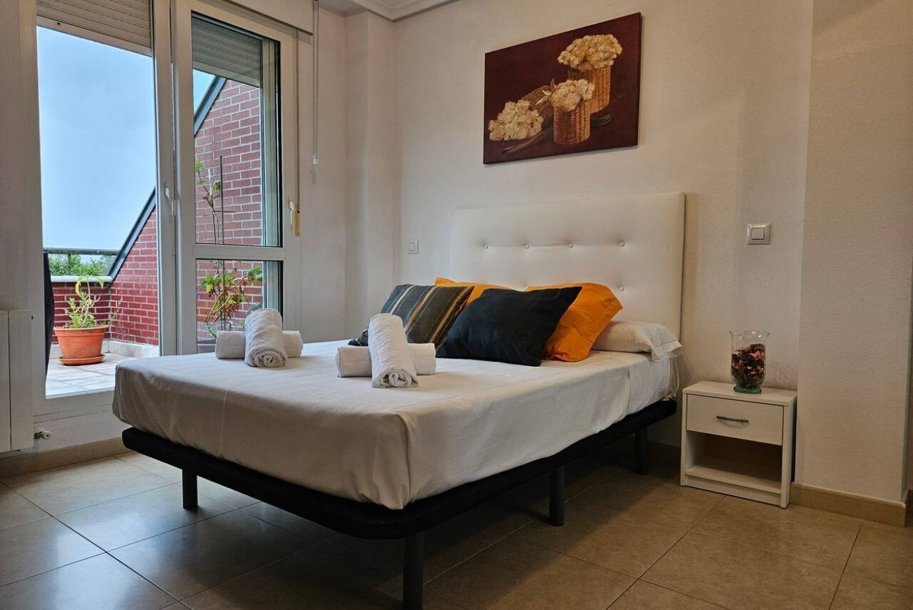 A bedroom with a bed, a nightstand, a window with a view of a brick building, and a painting on the wall.