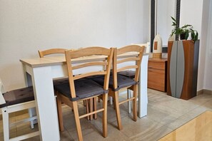 Un comedor con sillas de madera y una mesa blanca, un mueble con una planta y un panel decorativo en la pared.