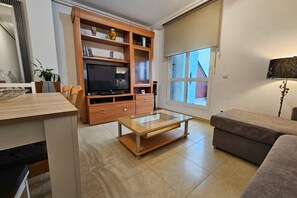 Un salon comprenant un téléviseur, un meuble de rangement en bois, une table basse en verre et un canapé.