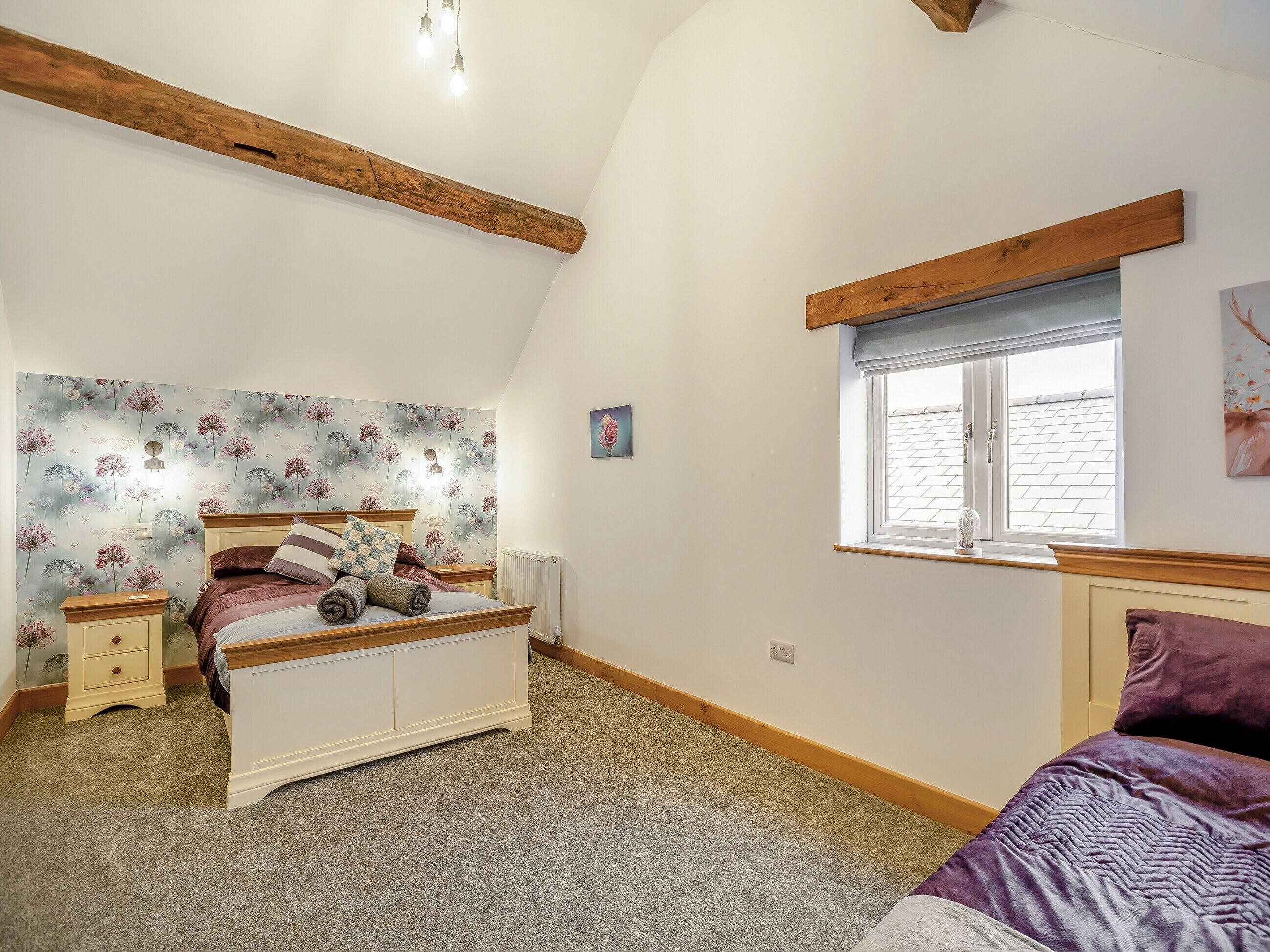Een slaapkamer met een bed, nachtkastjes, een radiator, een raam met uitzicht en een houten balk aan het plafond.