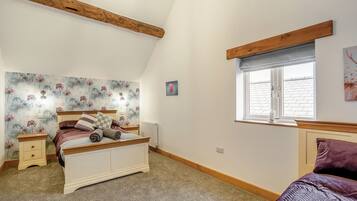 Een slaapkamer met een bed, nachtkastjes, een radiator, een raam met uitzicht en een houten balk aan het plafond.
