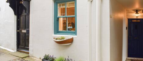 Un edificio blanco con una puerta azul, una ventana con marco azul y una pequeña maceta con plantas.