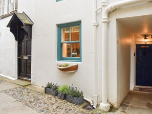 A white building with a blue door, a window with a blue frame, and a small window box with plants.