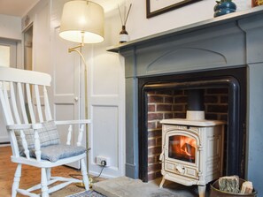 A cozy room with a white rocking chair, a white floor lamp, and a white wood-burning stove against a brick wall.
