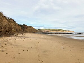 A sandy beach with cliffs and a distant view of a town.