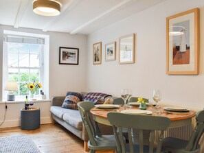 A dining area with a wooden table set for four, surrounded by chairs. A sofa with a plaid blanket is against the wall, and a window with blinds is visible. - 3 bedroom accommodation in Robin Hoods Bay, near Whitby (Robin Hoods Bay, near Whitby)