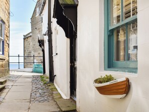 A narrow cobblestone path leading to a white building with a wooden boat planter on the wall.