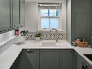 A kitchen with a white countertop, a sink, and a window with blinds.