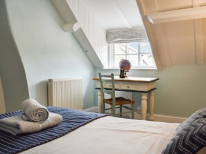 A bedroom with a sloped ceiling, a desk with a globe, a chair, a radiator, and a window with a view of the outside.