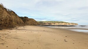 Uma praia de areia com falésias e uma vista distante de uma cidade.