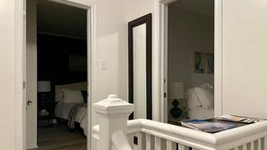 A hallway with a white railing, a door leading to a bedroom, and a table with magazines. - Center City with Recent Renos
(King & Double Beds) (St. John's)