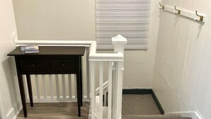 A staircase with a white railing, a dark wooden table with drawers, and a window with blinds. - Center City with Recent Renos
(King & Double Beds) (St. John's)