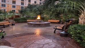 A courtyard with a stone fire pit, benches, and lush greenery. - 3BD/Vegas - Full Kitchen, Private Living Room, Pools and Hot Tubs! (Las Vegas)