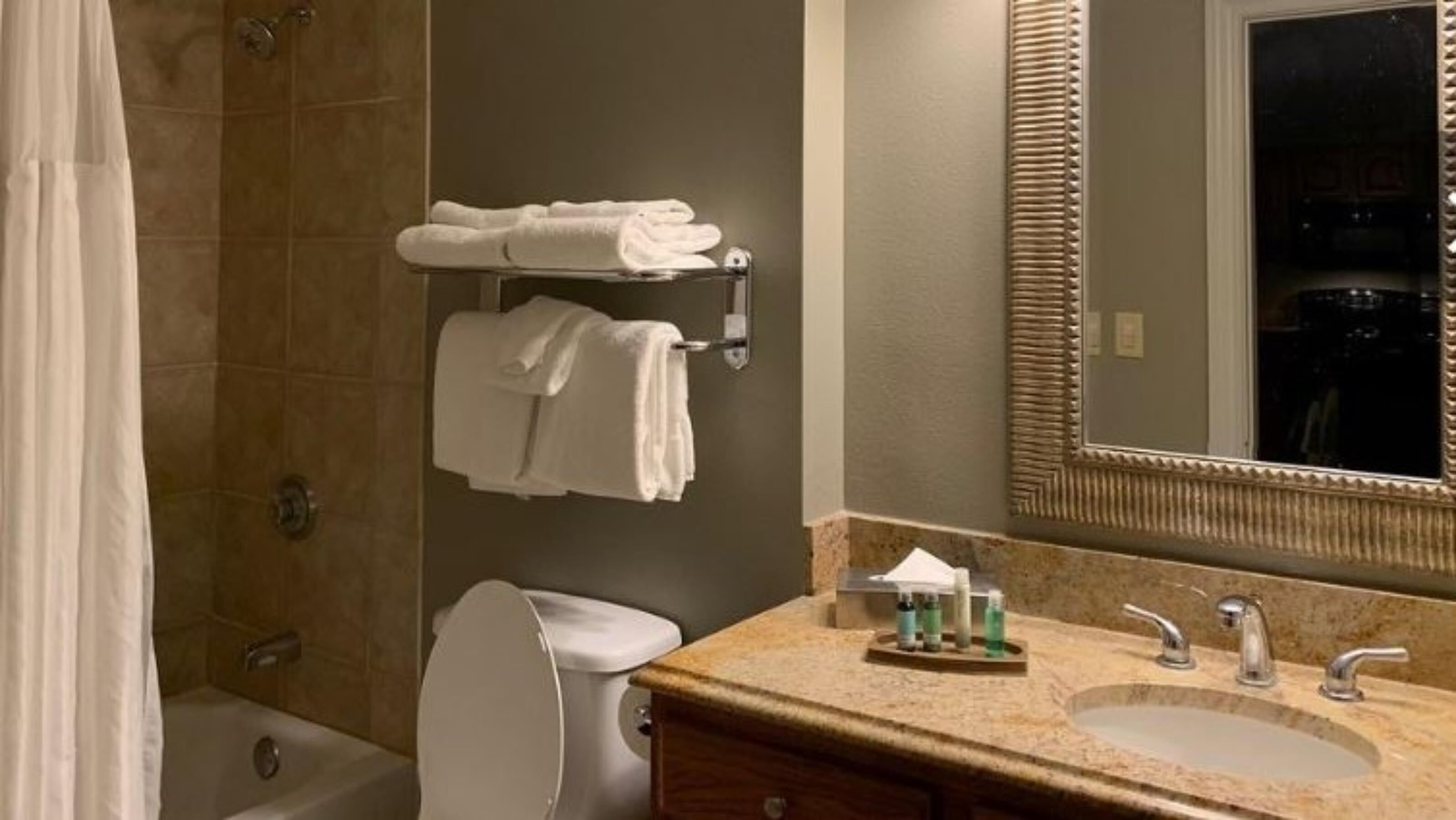 A bathroom with a shower, toilet, sink, and a towel rack with towels.