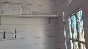 Un bagno con una parete bianca, un portasciuga, uno scaffale per asciugamani e una finestra con vetri colorati.