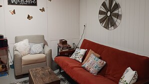 Una sala de estar con un sillón color beige, un sofá rojo y un reloj de pared.