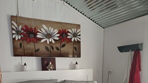 Un dormitorio con una cama, una obra de arte floral en la pared, cabecera blanca y una toalla roja colgada de un gancho.
