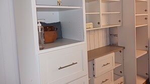 Un contenedor de almacenamiento blanco con múltiples estantes y cajones, algunos conteniendo objetos como una olla marrón y una botella de vidrio.