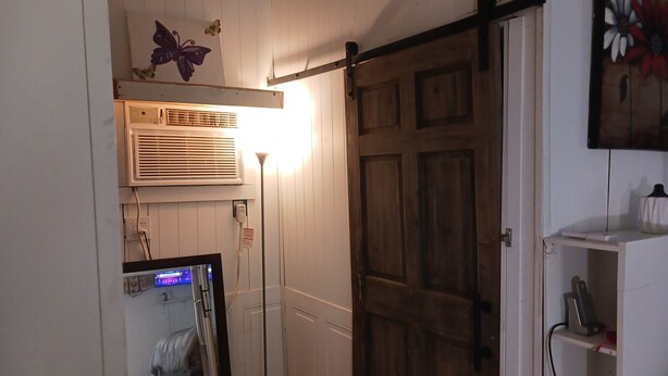 Una habitación con puerta de madera, espejo, equipo de aire acondicionado y lámpara de pie.