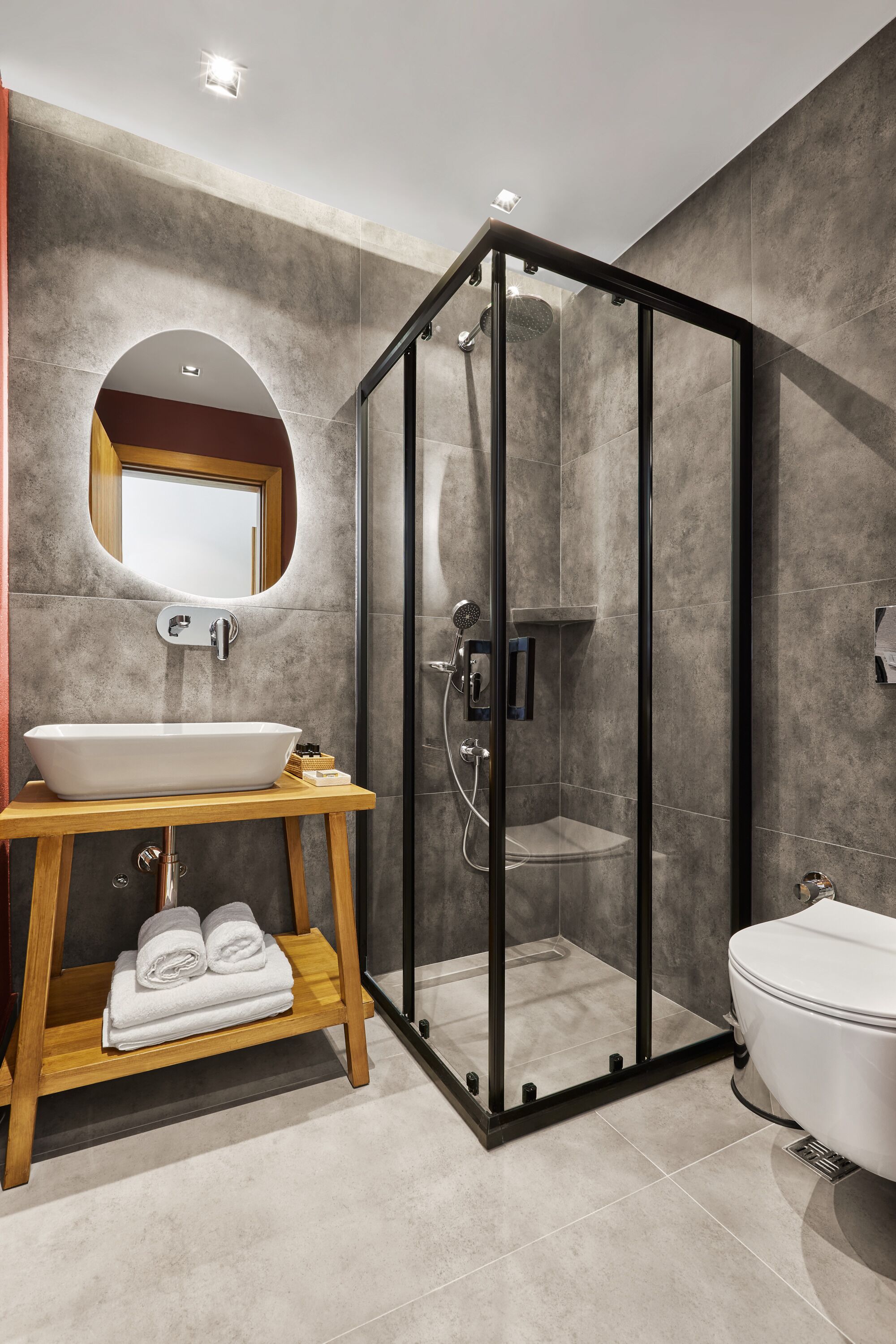 Un ba ño moderno con ducha envuelta en vidrio, tocador de madera con lavamanos y un inodoro.