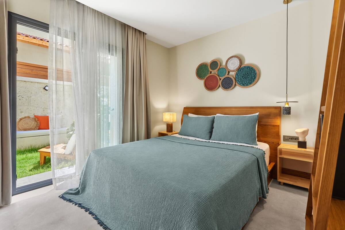 Une chambre moderne avec un grand lit, une tête de lit en bois, une table de chevet avec une lampe et un mur décoré d’assiettes.