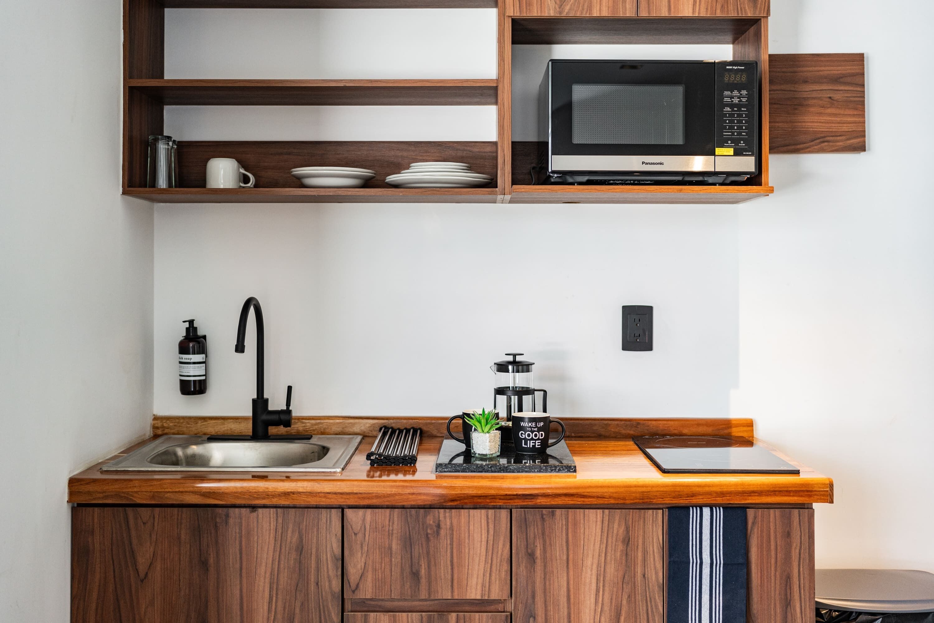 Een moderne keuken met houten kastjes, een roestvrijstalen spoelbak, een zwarte kraan, een magnetron, een koffiezetapparaat en een tablet op het aanrecht.