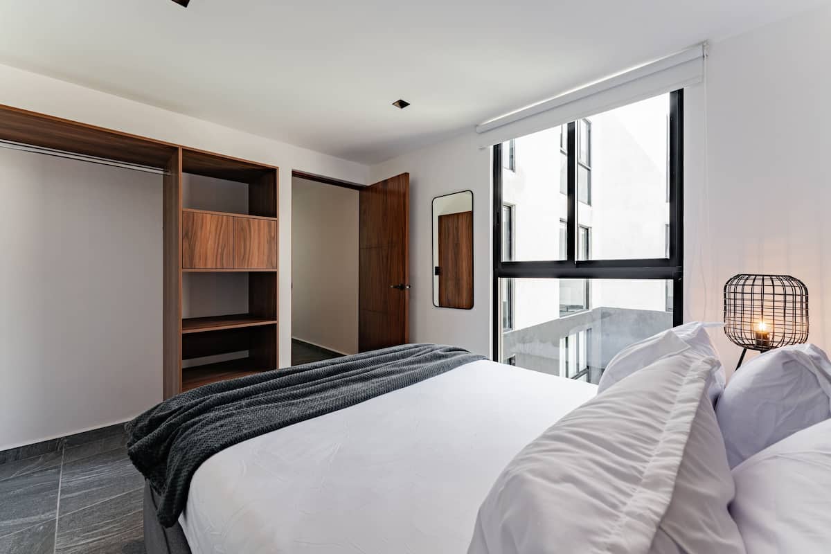 A modern bedroom with a large bed, a wardrobe, and a window with a view.