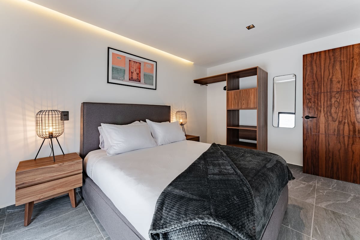 A modern bedroom with a bed, bedside tables, a wardrobe, and a framed picture on the wall.