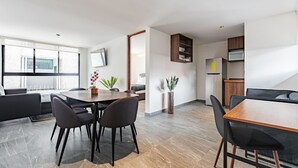 Een moderne woonkamer met een eethoek, keuken en een aan de muur bevestigde televisie.