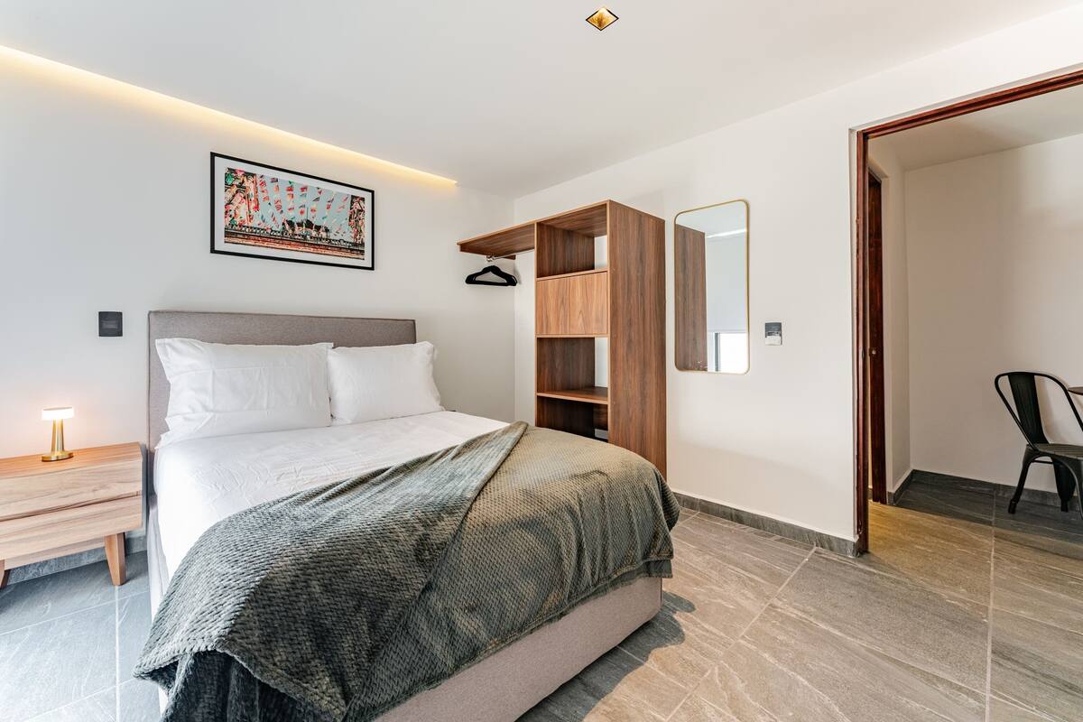 A modern bedroom with a bed, a wooden wardrobe, a mirror, and a nightstand.