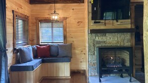 A cozy cabin interior with a built-in bench seating area, a stone fireplace, and a television mounted on the wall. - Boo Bear: New luxe lakeside cabin, hottub, caves, fast Wifi @ BearTrackLake (Beattyville)