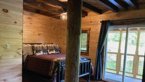 A wooden cabin bedroom with a bed, a window with curtains, and a view of greenery outside. - Boo Bear: New luxe lakeside cabin, hottub, caves, fast Wifi @ BearTrackLake (Beattyville)