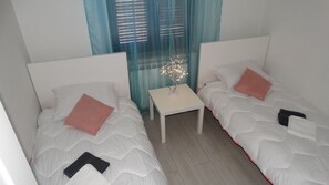 Two single beds with pillows and blankets, a small table, and a decorative light fixture.