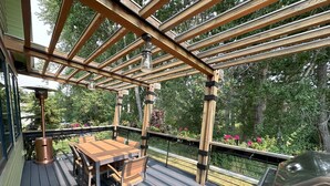 Une terrasse en bois avec une table et des chaises, un barbecue et une pergola agrémentée d’un luminaire suspendu.