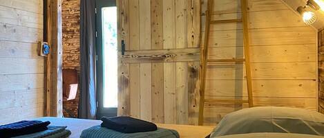 A cozy attic bedroom with wooden walls, a loft bed, and a ladder.