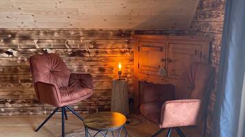 Une pièce chaleureuse aux murs et au plafond en bois, comprenant deux fauteuils confortables, une petite table ronde et un luminaire central.
