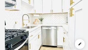 Una cocina moderna con armarios blancos, tiradores dorados, un lavavajillas de acero inoxidable y una estufa a gas negra.