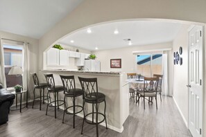 A modern kitchen with a central island, bar stools, and a dining area with a table and chairs. - Charming "Home Away From Home" (Las Cruces)