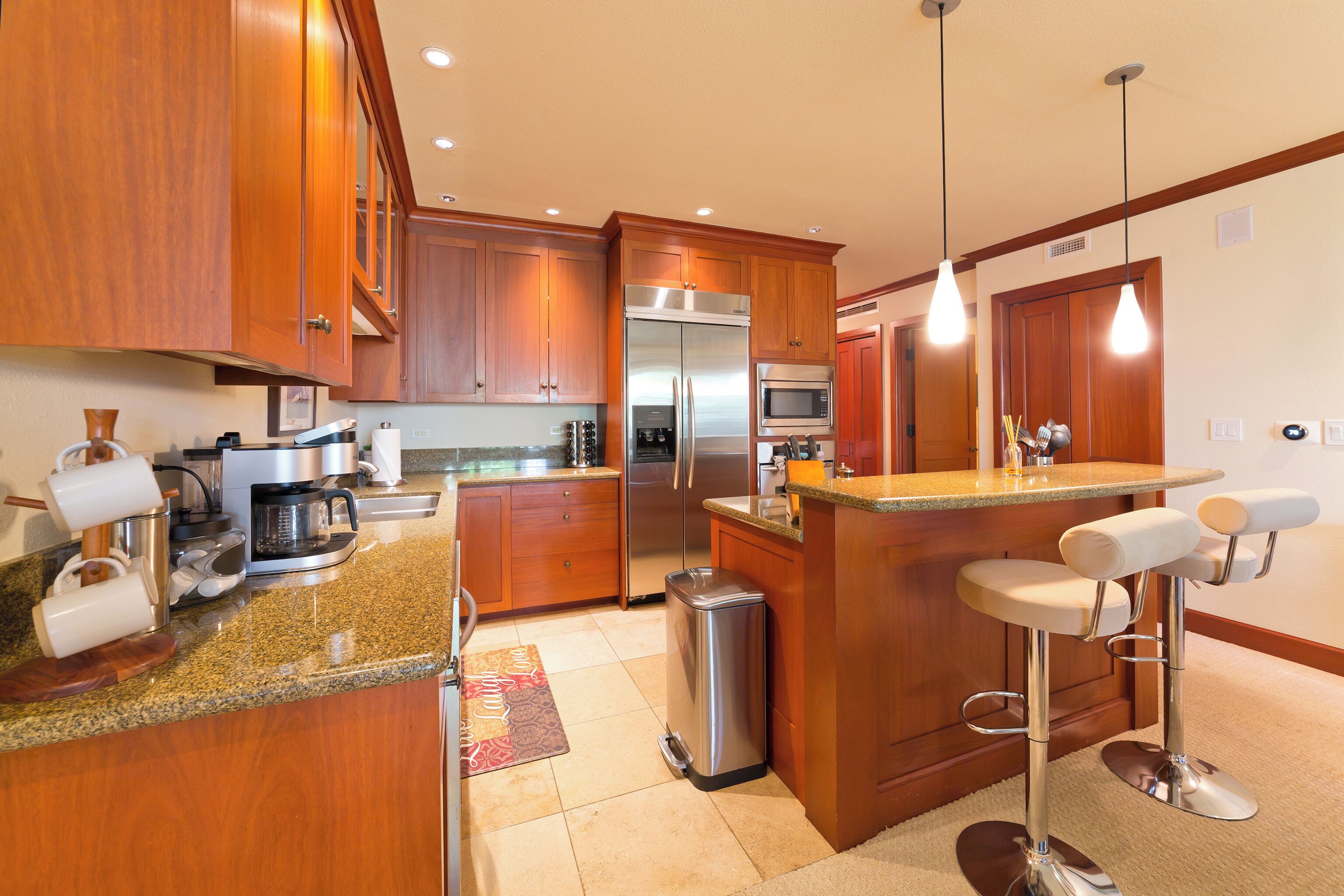 A modern kitchen with wooden cabinets, stainless steel appliances, a granite countertop, and a bar area with stools.
