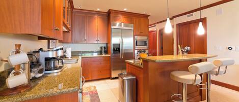 A modern kitchen with wooden cabinets, stainless steel appliances, a granite countertop, and a bar area with stools.