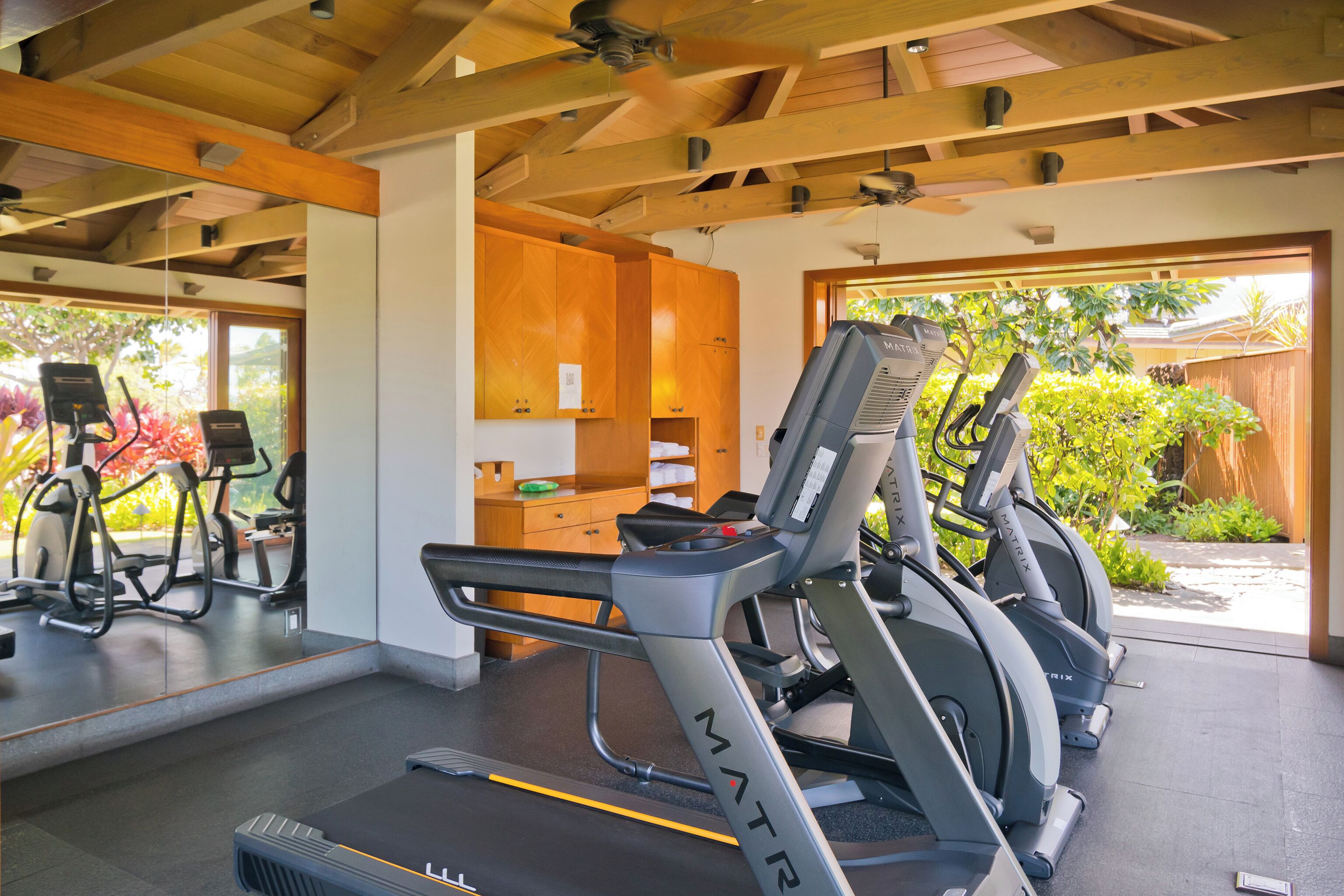 Une salle de sport équipée de tapis de course, de vélos d’exercice et dotée d’un plafond en bois.