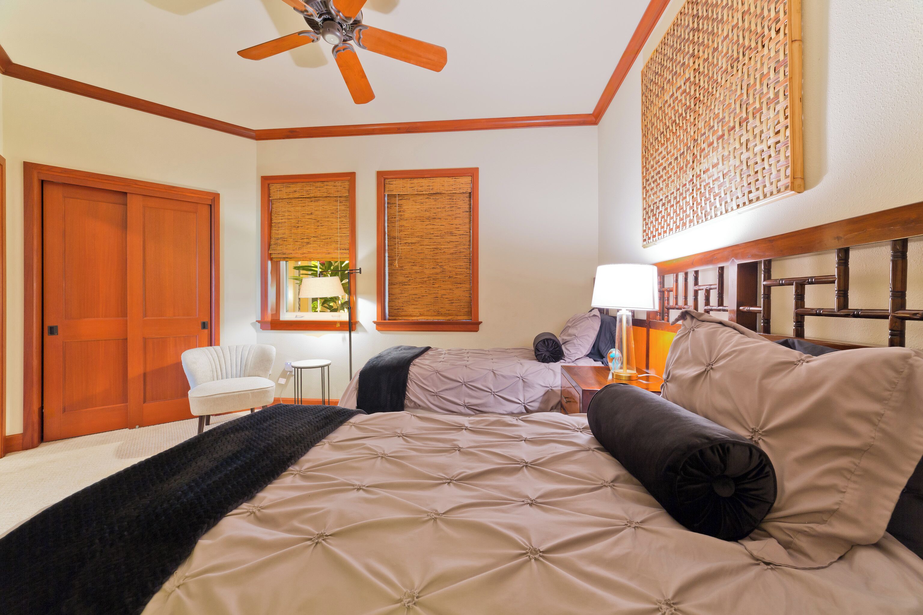 A bedroom with a large bed, a ceiling fan, wooden doors, and a window with blinds.