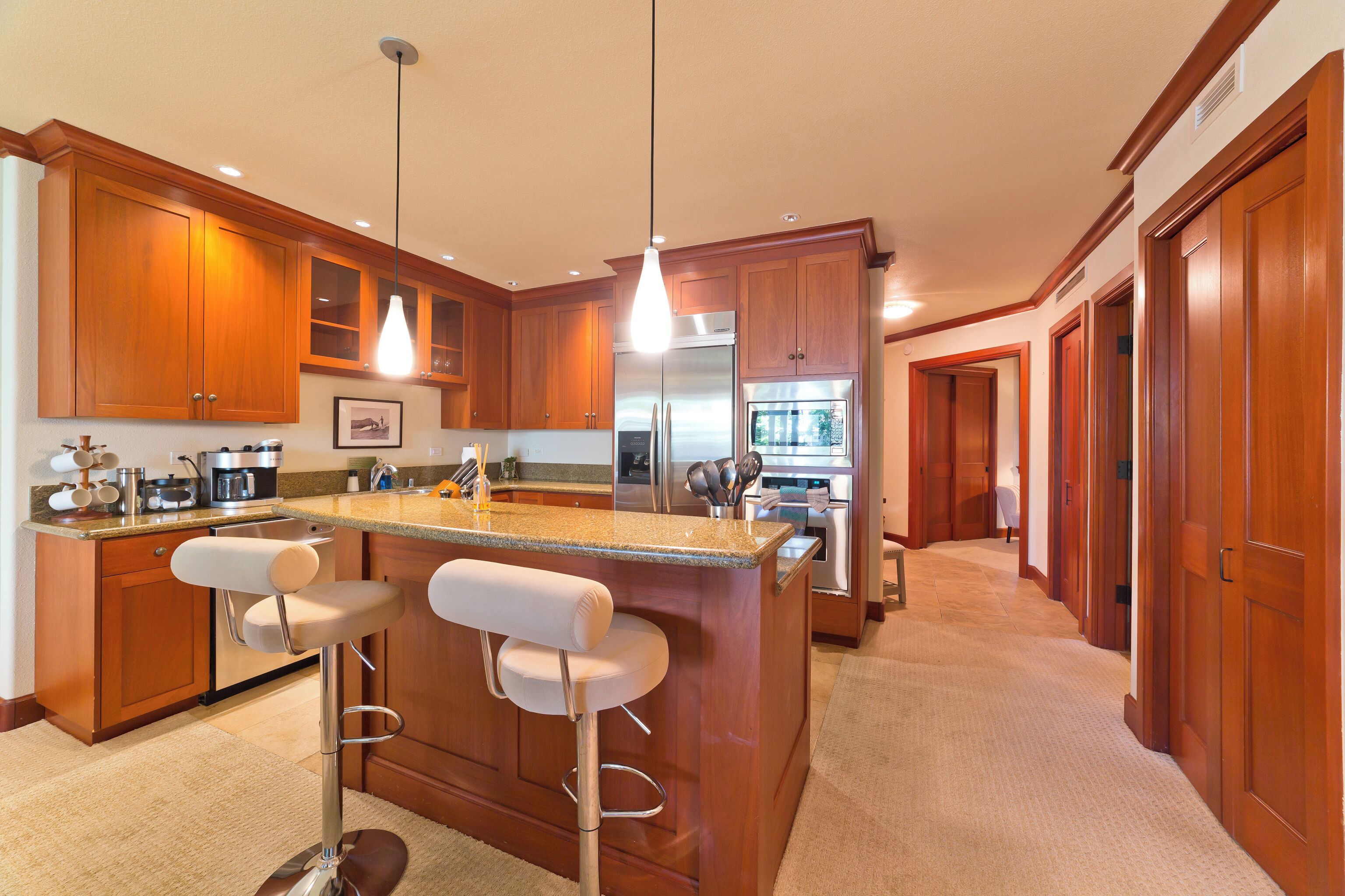A modern kitchen with wooden cabinets, a stainless steel refrigerator, and a bar area with stools.